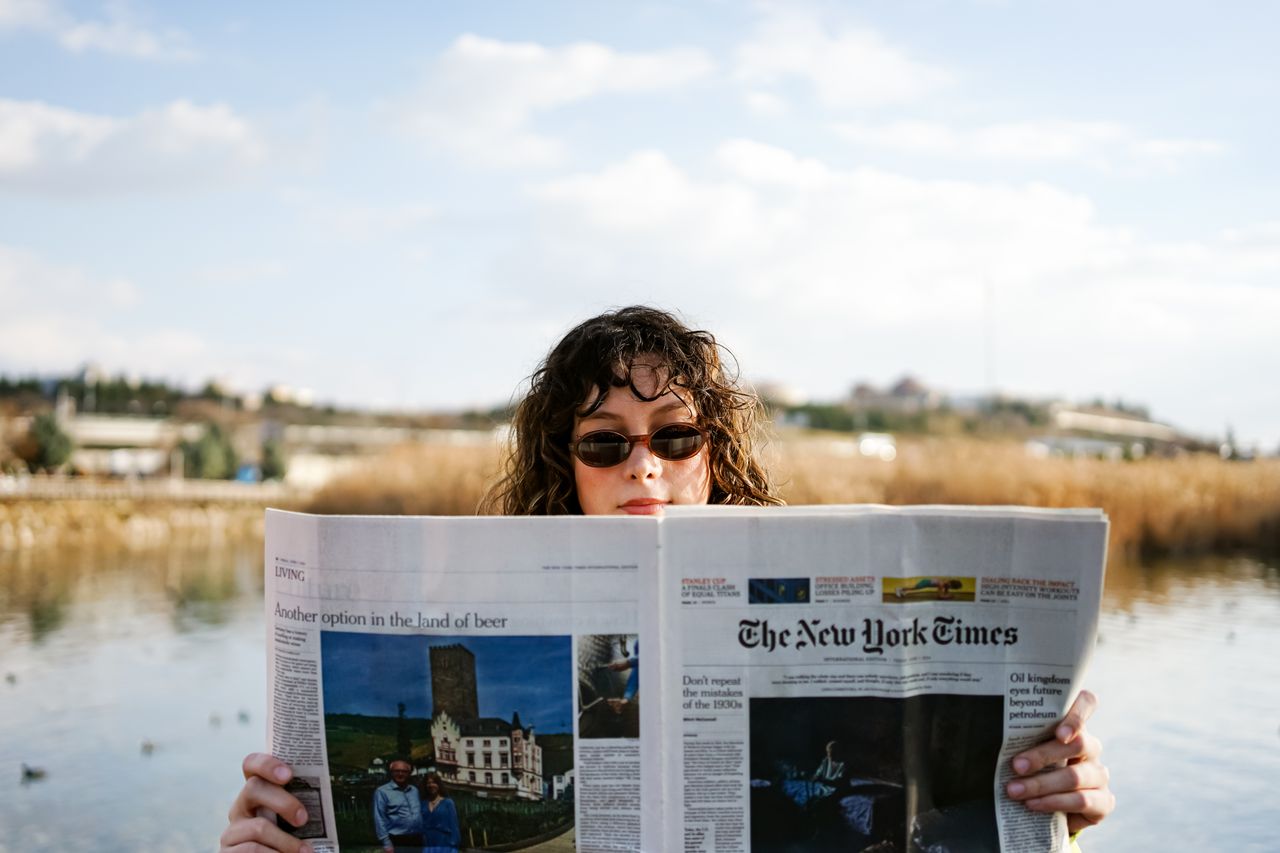 A woman reading The New York Times while enjoying a sunny day by a lake.